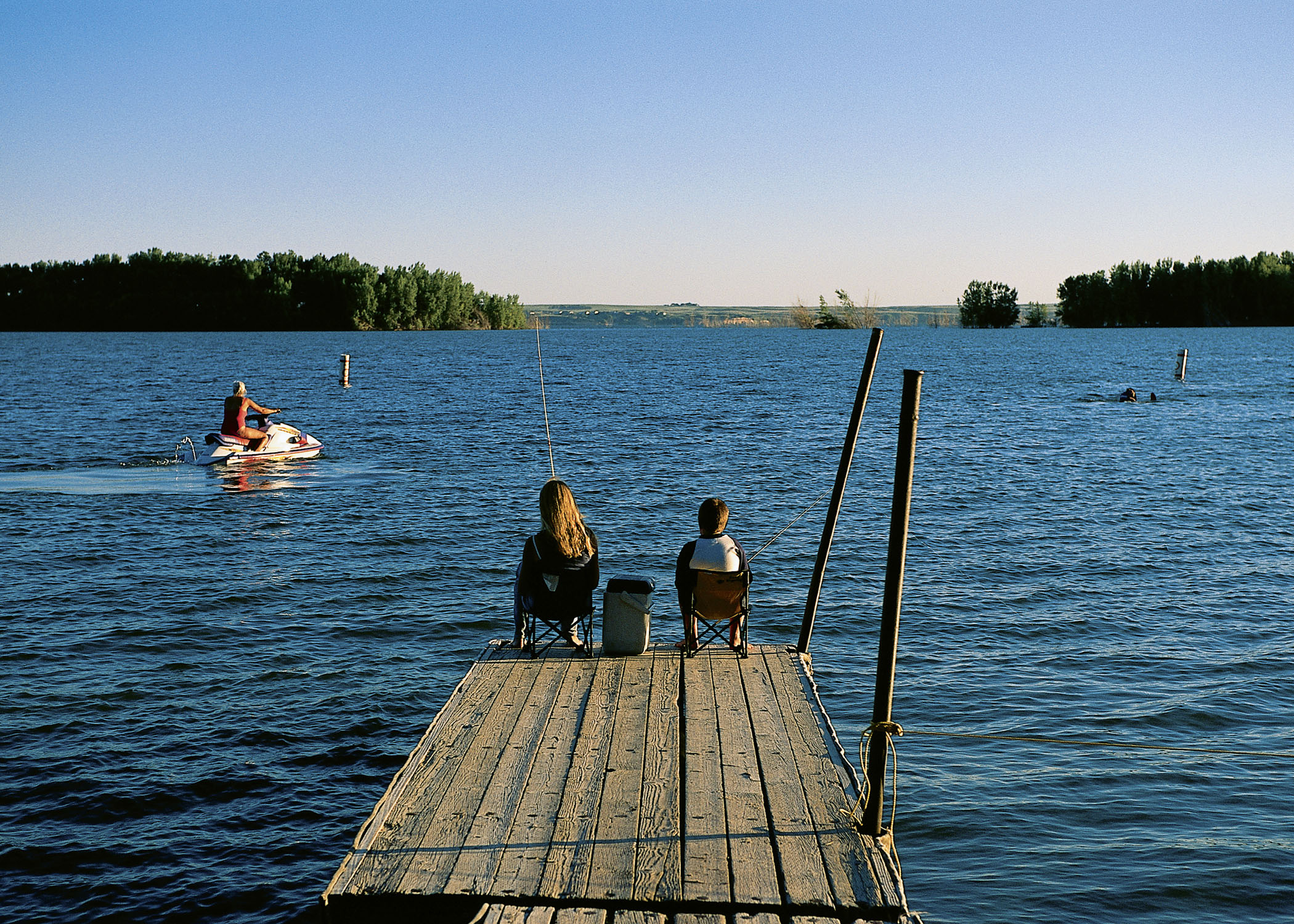 Two kids sit in lawn chairs and fish from a wooden dock at Lake McConaughy in Nebraska.