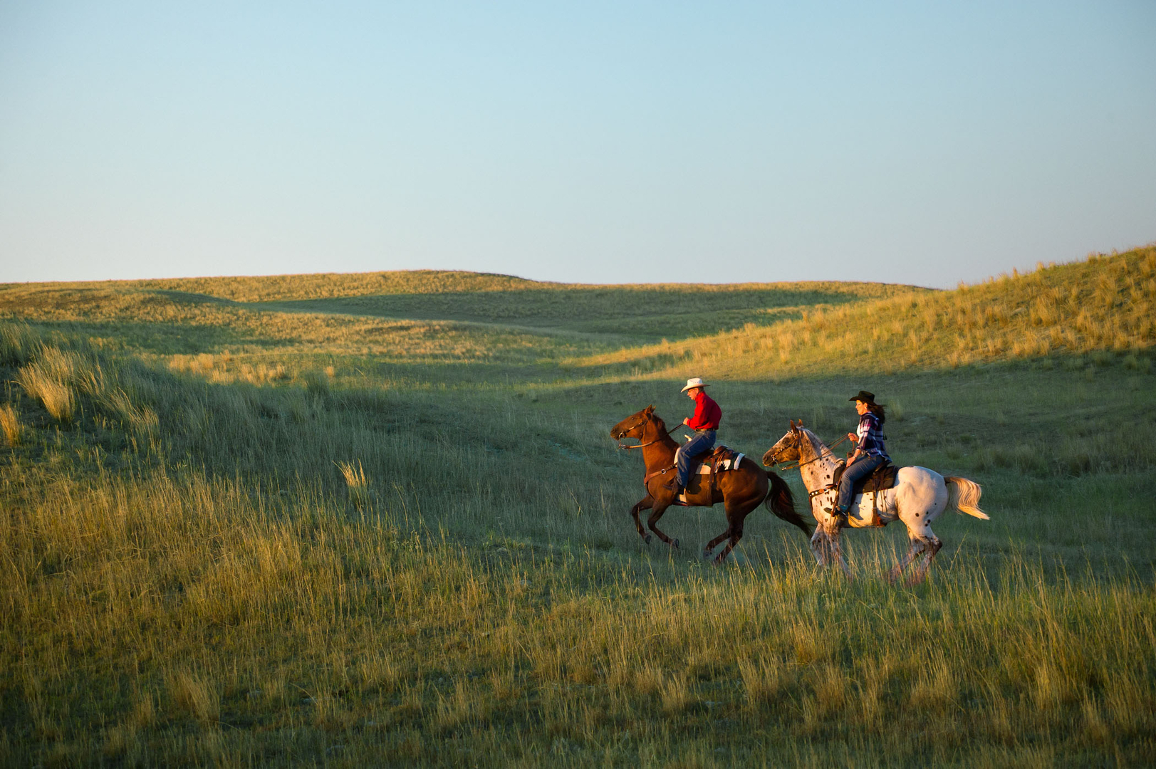 Two people on horses with a scenic view of the Sandhills in the background.