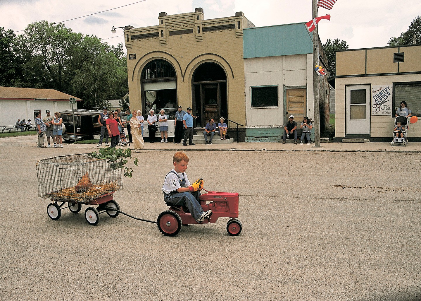 A  book riding a tiny tracker with a caged chicken behind him on a wagon in front of a crowd at Grundlovsfest.