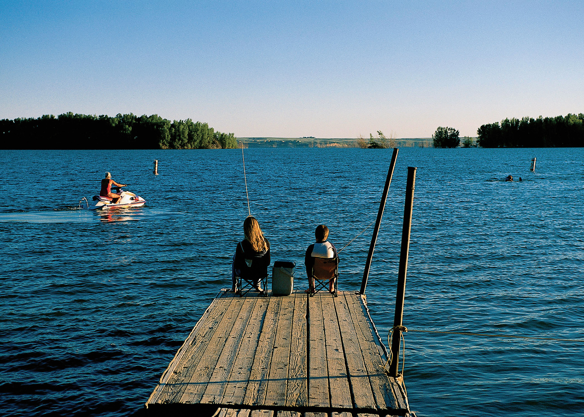 Two people fishing from a pier at Lake McConaughy State Recreation Area with someone on a Jet Ski in the water.
