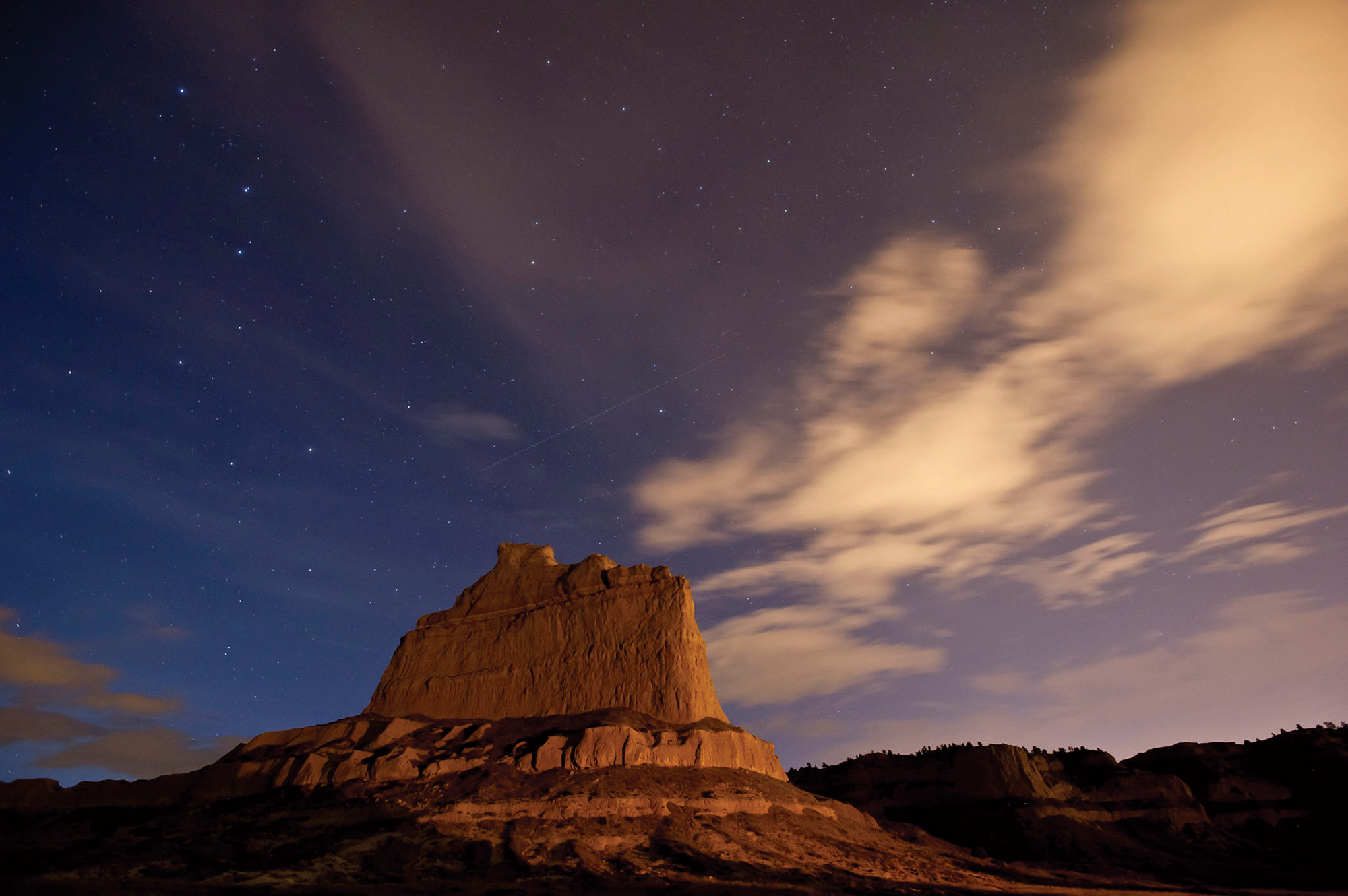 A large rocky outcrop stretching towards the starry sky at Scotts Bluff National Monument at night. 