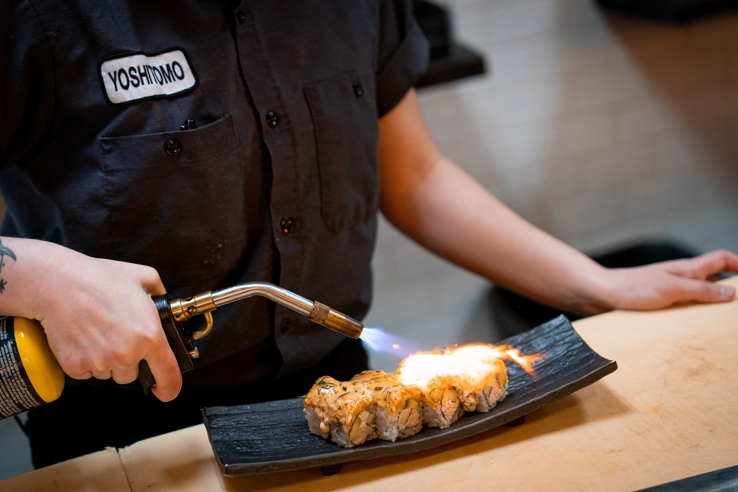A chef using a blow torch to char fish atop a sushi roll at Yoshitomo.