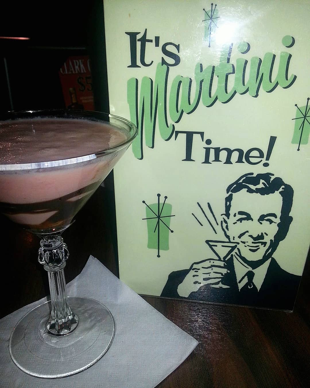 A cocktail next to a vintage flyer of a man holding a martini that says "Martini Time" at Lincoln's Starlight Lounge.